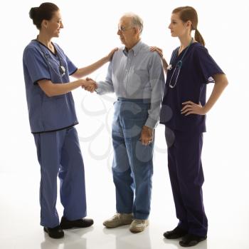 Royalty Free Photo of a Woman in Scrubs Shaking the Hand of an Elderly Man While Another Doctor has Her Hand on His Shoulder