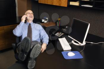 Royalty Free Photo of a Businessman Sitting at His Desk Talking on a Cellphone