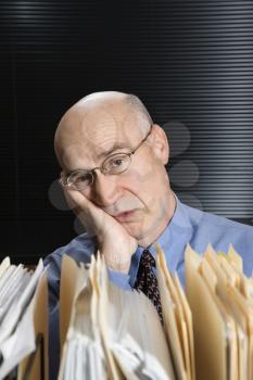 Royalty Free Photo of a Middle-Aged Businessman With Files Leaning Head on Hand Looking Tired