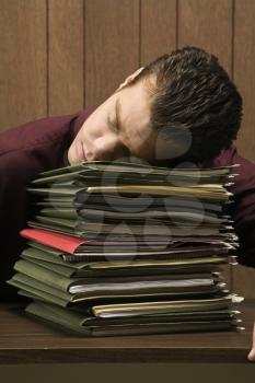 Royalty Free Photo of a Businessman Sitting at a Desk Resting His Head on a Tall Stack of Folders