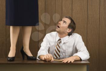 Royalty Free Photo of a Man Sitting at a Desk Looking Up to Woman Standing on a Desk