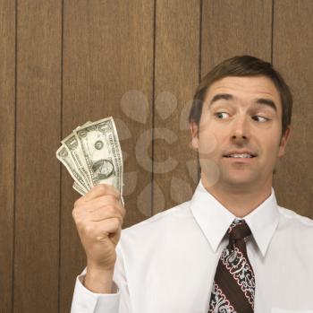 Mid-adult Caucasian male holding dollar bills and looking towards them.