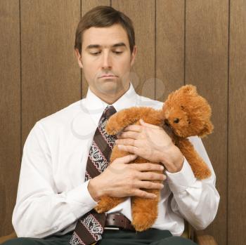 Royalty Free Photo of a Businessman Holding a Stuffed Animal Looking Sad