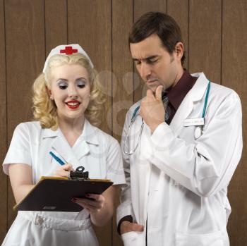 Royalty Free Photo of a Nurse and Doctor Standing Looking at a Clipboard