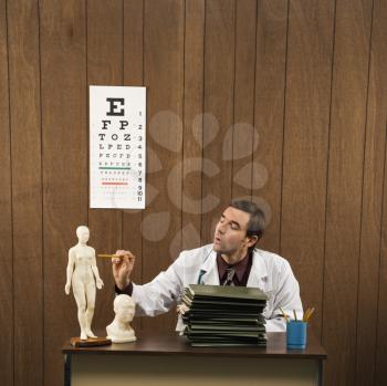 Royalty Free Photo of a Male Doctor Sitting at a Desk Pointing to a Figurine
