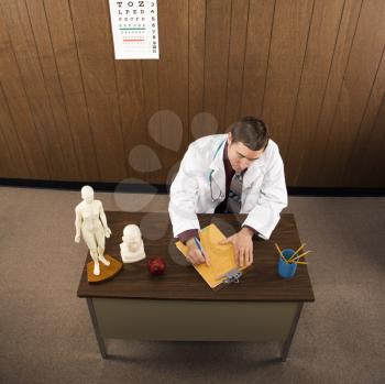 Royalty Free Photo of a High Angle of a Male Doctor Sitting at a Desk Writing