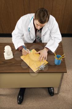 High angle of mid-adult Caucasian male doctor at desk writing.