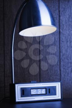 Royalty Free Photo of a Dim Desk Lamp and Retro Clock Against Wood Paneling at Night