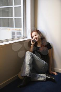 Royalty Free Photo of a Pretty Redheaded Woman Sitting on the Floor by a Window Talking on a Cellphone