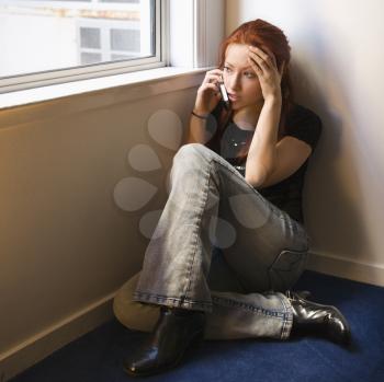 Royalty Free Photo of a Pretty Redheaded Woman Sitting on the Floor by a Window Talking on a Cellphone