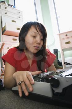 Royalty Free Photo of a Young Woman Lying on the Floor in a Red Robe Typing on a Typewriter