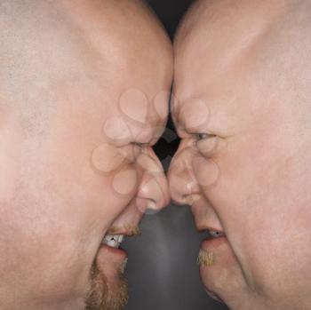Royalty Free Photo of Identical Twin Men Standing Face to Face With Angry Expressions