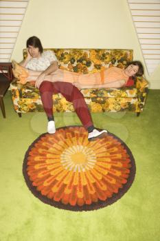 Royalty Free Photo of a Woman Lying on a Colorful Retro Sofa With Legs Draped Over a Man