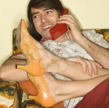 Royalty Free Photo of a Man Talking on the Telephone With a Woman's Legs Draped Over His Lap