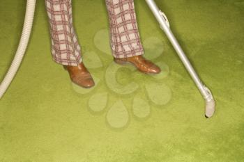 Royalty Free Photo of a Close-Up of a Man's Feet With a Vacuum Extension Against a Green Retro Carpet