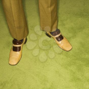 Close-up of Caucasian mid-adult male feet in vintage shoes against green rug.