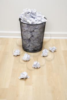 Royalty Free Photo of a Wire Mesh Trash Can With Crumpled Paper Scattered Around