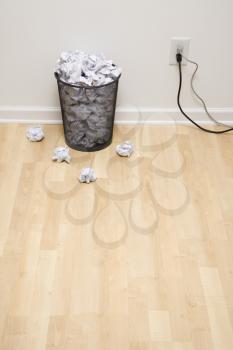 Royalty Free Photo of a Full Wire Mesh Trash Can With Crumpled Paper Next to an Electrical Outlet and Plugs