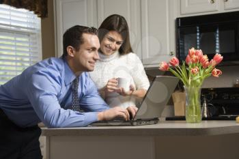 Royalty Free Photo of a Couple in a Kitchen With Coffee Looking at a Laptop Computer