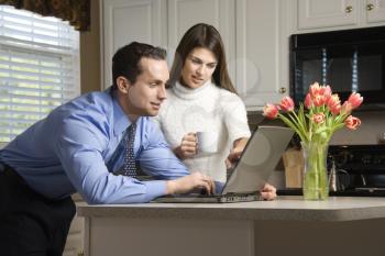 Royalty Free Photo of a Couple in a Kitchen With Coffee Looking at a Laptop Computer