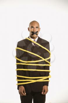 Royalty Free Photo of a Businessman Wrapped in a Yellow Rope With Tape Over His Mouth