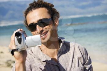 Mid-adult Caucasian man on beach pointing video camera at viewer.
