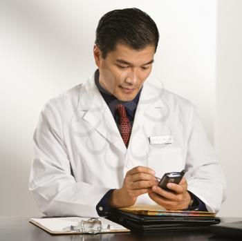Royalty Free Photo of a Doctor Sitting at a Desk With Charts Using a PDA