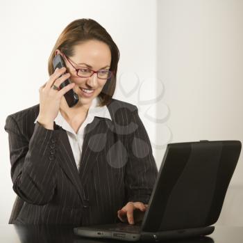 Royalty Free Photo of a Businesswoman Sitting at a Desk Smiling With Laptop Computer Talking on a Cellphone
