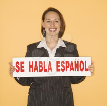 Caucasian businesswoman smiling holding sign reading 'se habla espanol.'