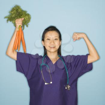 Royalty Free Photo of a Female Doctor Flexing Muscles and  Holding up a Bunch of Carrots