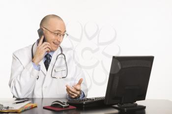 Royalty Free Photo of a Physician Sitting at a Desk With a Computer, Talking on a Cellphone