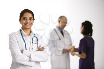 Indian mid adult woman doctor standing with medical staff in background.
