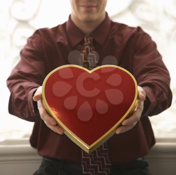 Royalty Free Photo of a Man Holding a Heart Shaped Box of Chocolates Out
