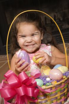 Hispanic girl holding egg from Easter basket looking at viewer smiling.