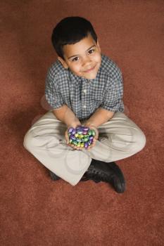 Royalty Free Photo of a Boy Sitting on the Floor Holding Chocolate Candy Eggs in His Hands Smiling