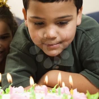 Royalty Free Photo of a Boy Looking Down Wishfully at Lit Candles of a Birthday Cake With Girl Peeking in Over His Shoulder