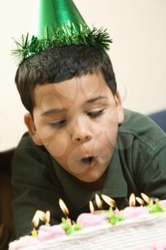 Royalty Free Photo of a Boy Wearing a Party Hat Blowing Out Candles on a birthday Cake