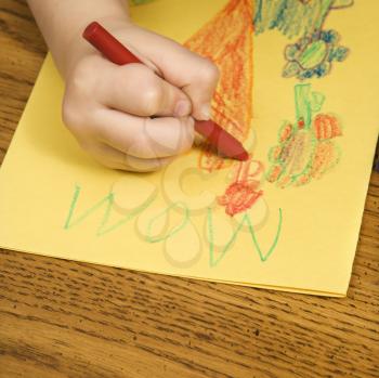 Royalty Free Photo of a Boy Drawing on Yellow Paper With Crayons