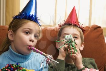 Royalty Free Photo of Children Looking Bored Wearing Party Hats and Blowing Noisemakers