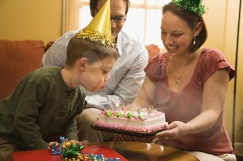 Royalty Free Photo of a Boy in a Party Hat Blowing Out Candles on a Birthday Cake
