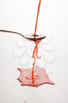 Royalty Free Photo of a Stream of Red Cough Syrup Overflowing Spoon Into a Puddle Below