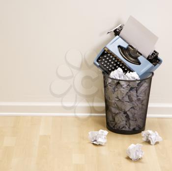 Royalty Free Photo of a Typewriter in a Trash Can Surrounded by Crumpled Paper