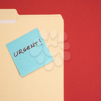 Royalty Free Photo of a Folder With a Blue Sticky Note Attached Reading Urgent