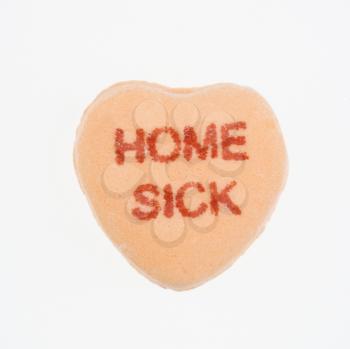Orange candy heart that reads home sick against white background.