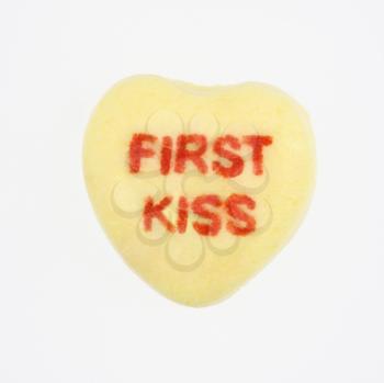 Royalty Free Photo of a Yellow Candy Heart That Reads First Kiss