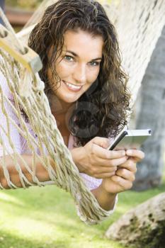 Royalty Free Photo of a Smiling Pretty Woman Lying in a Hammock Using PDA