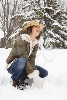 Caucasian young adult female kneeling in the snow wearing straw cowboy hat and smiling.