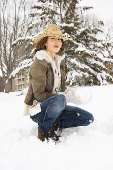 Royalty Free Photo of a Woman Kneeling in the Snow With a Snowball and Wearing a Cowboy Hat