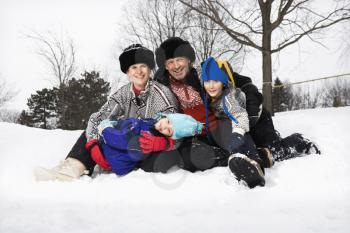 Portrait of happy Caucasian family of four sitting in snow smiling at veiwer.