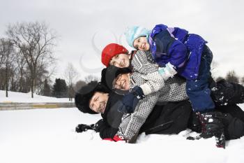 Royalty Free Photo of a Happy Family of Four Lying Stacked on Top of Each Other in Snow